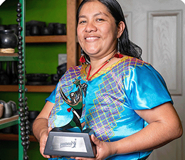Magali Pedro en 2024, con trofeo en mano y blusa tradicional en una tienda de cerámica.